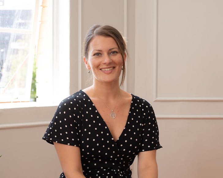 Nikki Goodson, Founder of Impact Digital smiles. She wears a black and white polka dot dress and a necklace of a tree. 