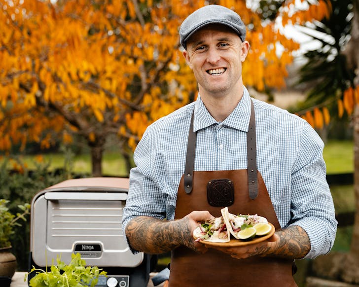 The tattooed butcher shows us a plate of food he cooked in the Ninja Woodfire Outdoor Oven.