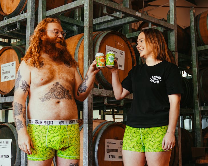 A man and a woman wearing underwear with a pickle print on them toast with cans of Pickle Beer. 