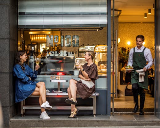 Two people sitting outfront of a deli. 