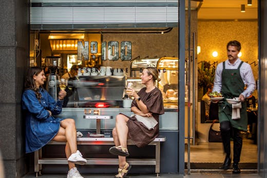 Two people sitting outfront of a deli.