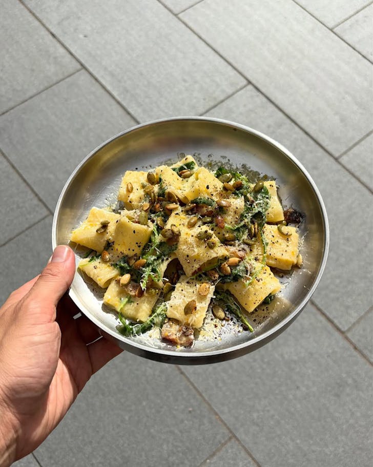 Somebody carries a flattish silver plate of pasta. 