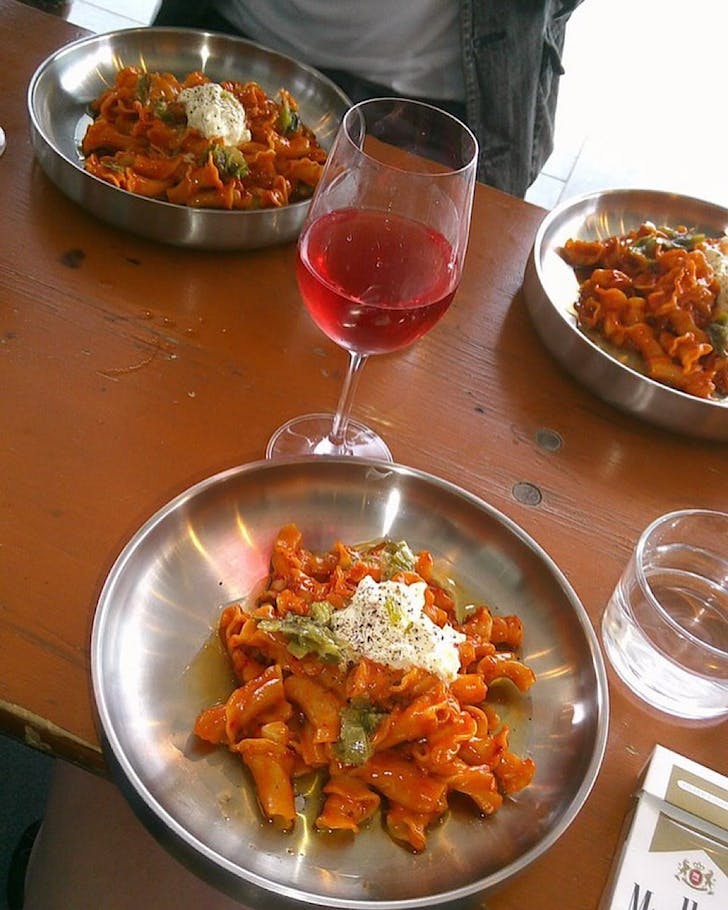 A flattish silver plate of pasta and a glass of wine. 