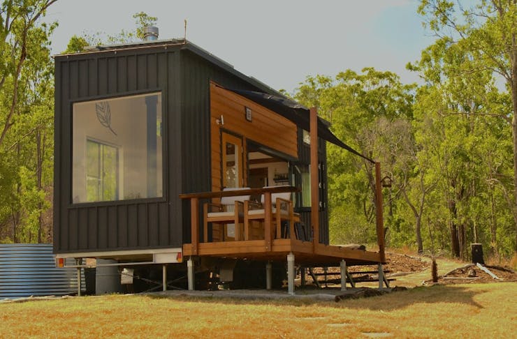 Tiny home with large window and front deck, in bushland.