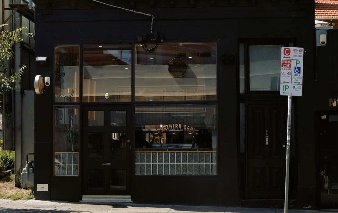 A black painted store with a parking sign out front. 