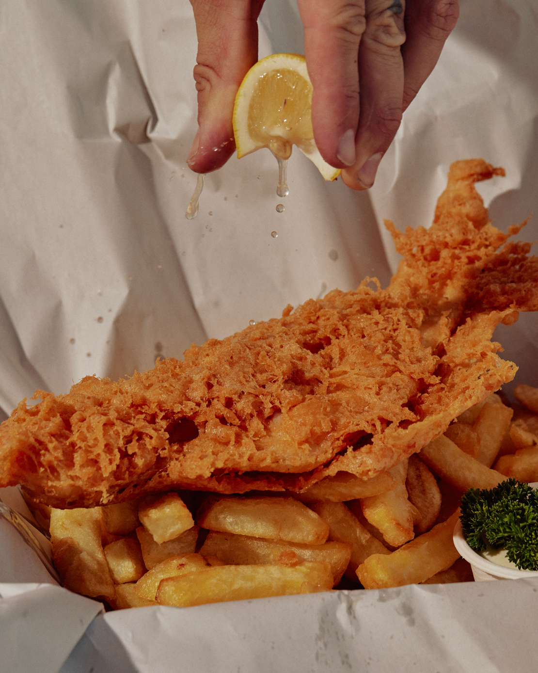 A person squeezing lemon onto fried fish at a fish and chips shop Melbourne.