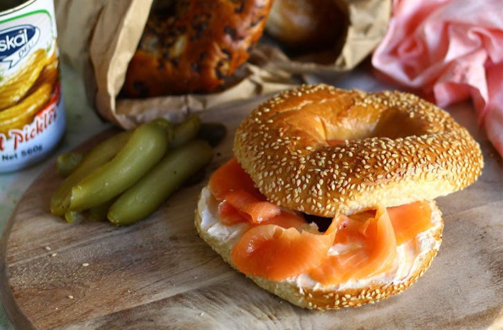A Melbourne best bagel sits on a chopping board loaded with cream cheese and smoked salmon.
