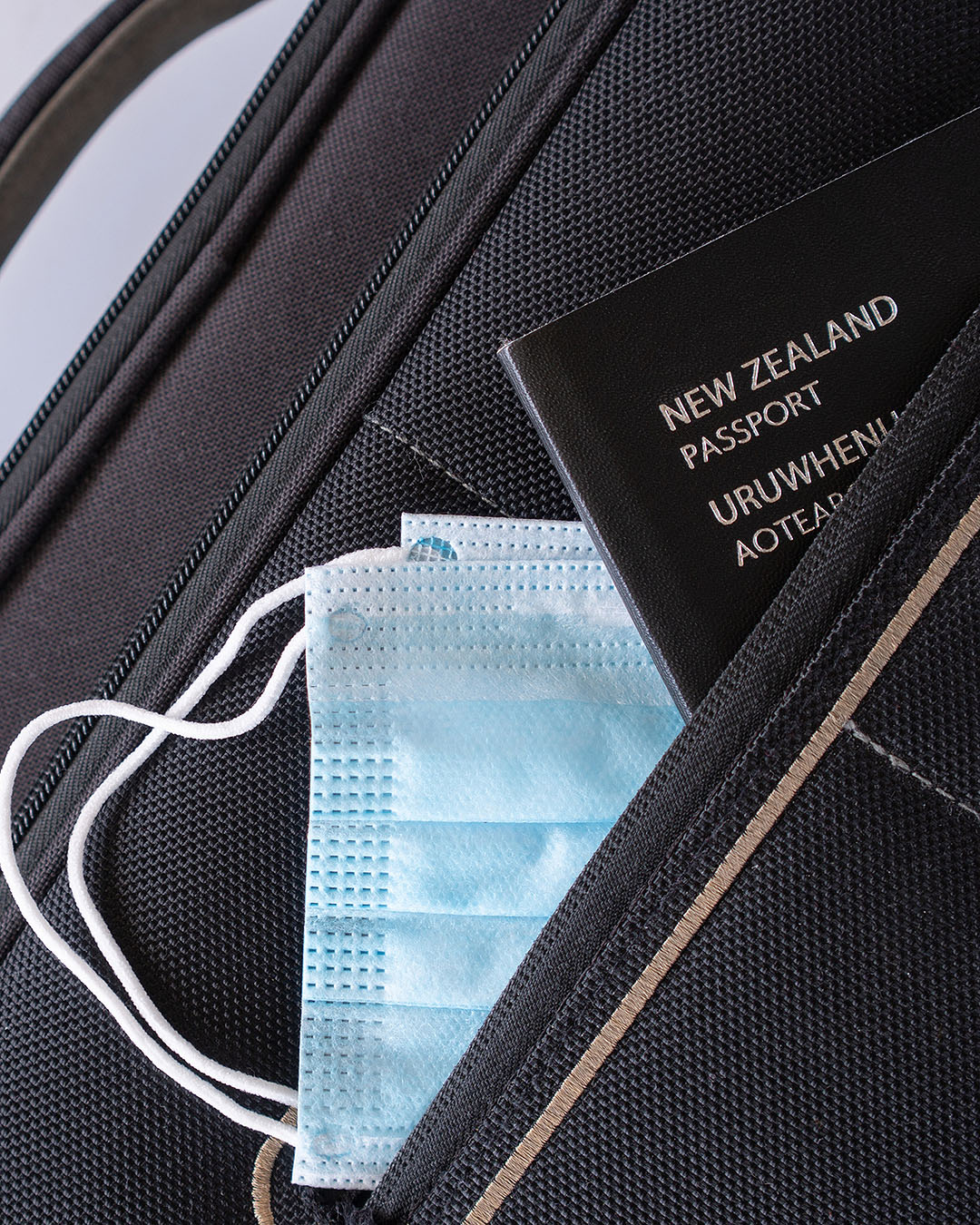 A NZ passport with masks peeking out of luggage.