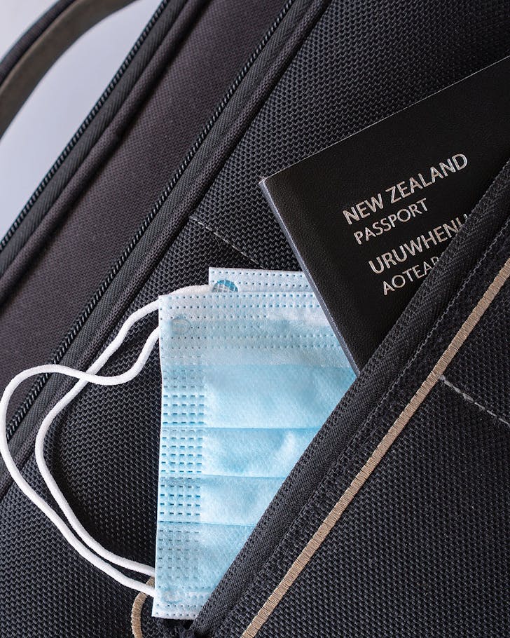 A NZ passport with masks peeking out of luggage.