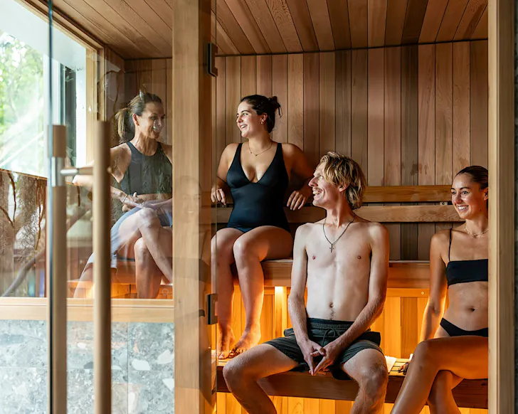 A group of happy people sit in an aesthetic traditional sauna at O-Studio in Remuera.