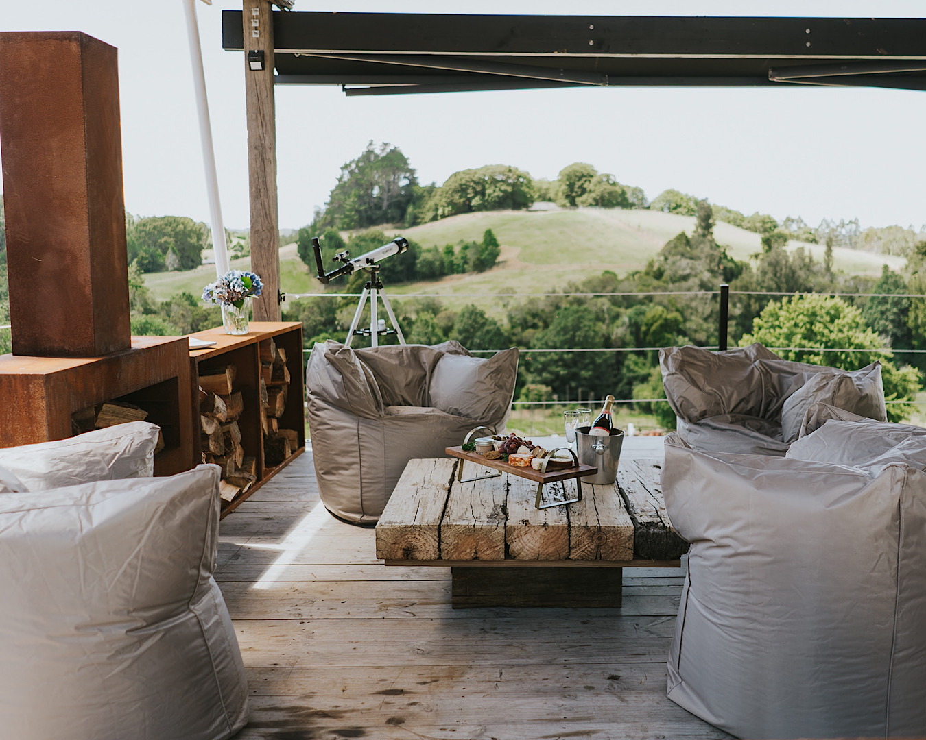 Luxe beanbag chairs sit around a wooden table topped with an elegant cheeseboard and champagne at Oakridge Glamping in Rotorua. 