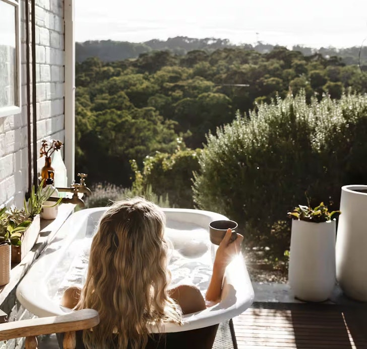A woman lounges in the outdoor bath looking at the view at Ode to the Orchard one of the best Airbnbs near Adelaide