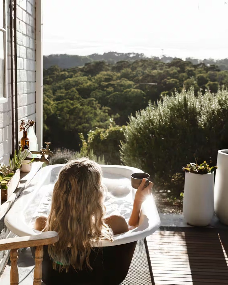 A woman lies in the outdoor bath looking at the view at Ode to the Orchard one of the best romantic getaways in Australia