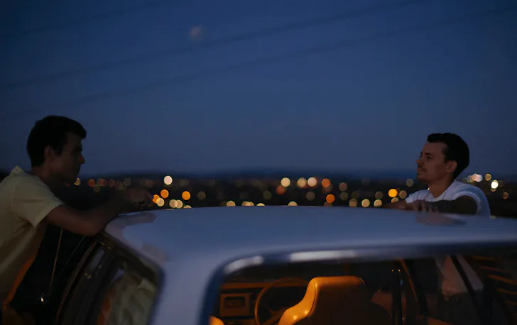 Two people talking over a car at sunset. 