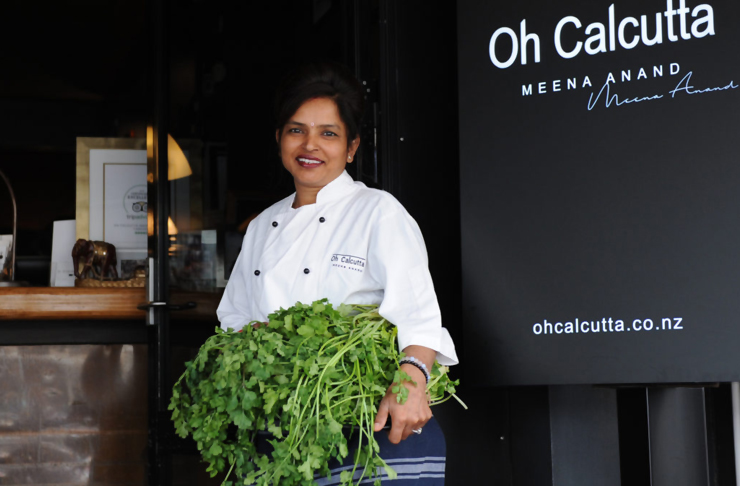 Meena, the Executive Chef of Oh Calcutta stands in front of her restaurant smiling with a bushel of herbs
