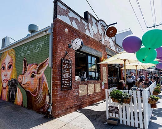 The exterior to Old Garage Cafe, a brick building with tables out-front and a window for take-away coffee. 