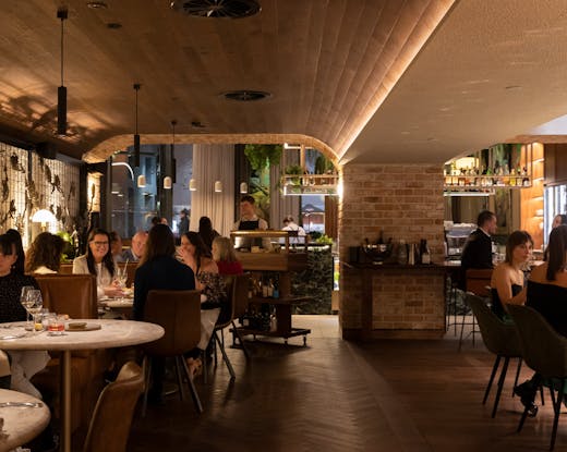 A busy restaurant with people dining and white-shirted waiters walking. 