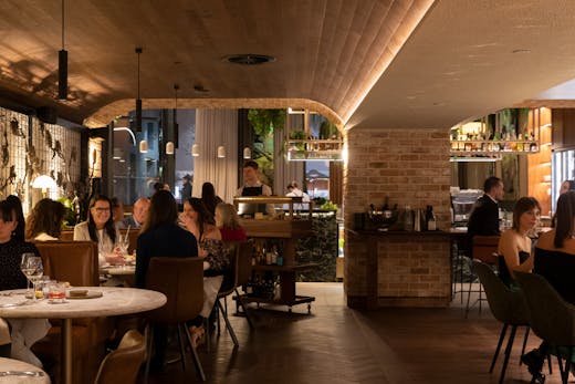 A busy restaurant with people dining and white-shirted waiters walking.