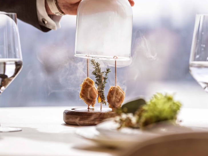 A server presenting smoked chicken on skewers at Oncore by Clare Smyth, Crown Sydney