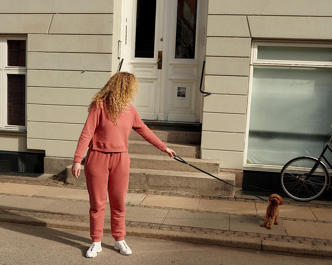 A woman wearing head-to-toe activewear label Organic Basics attempts to convince her tiny puppy to go for a walk. 