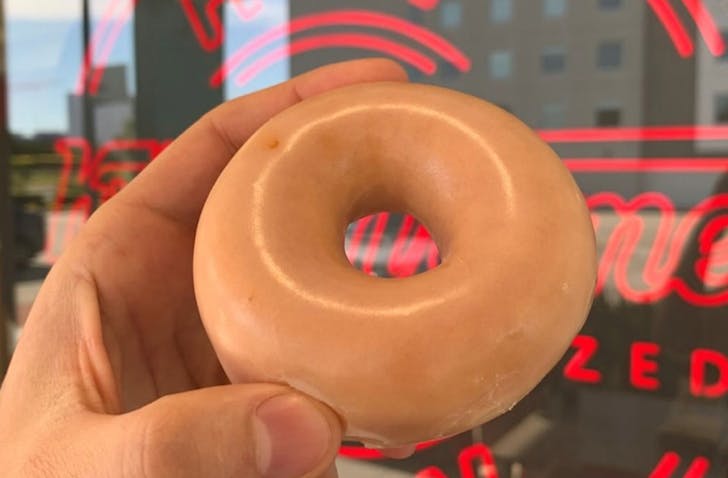 Original Glazed Doughnut held in front of sign