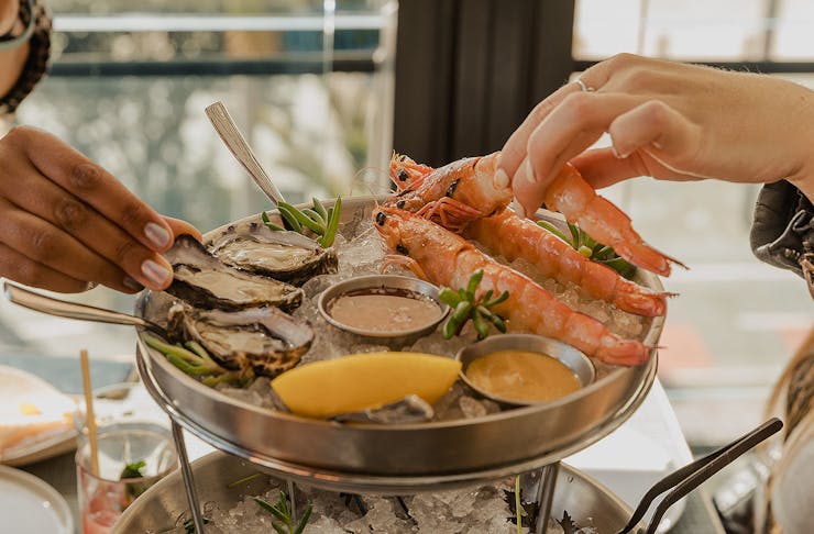 Hands reach for seafood at Origine, one of the best restaurants in Auckland.