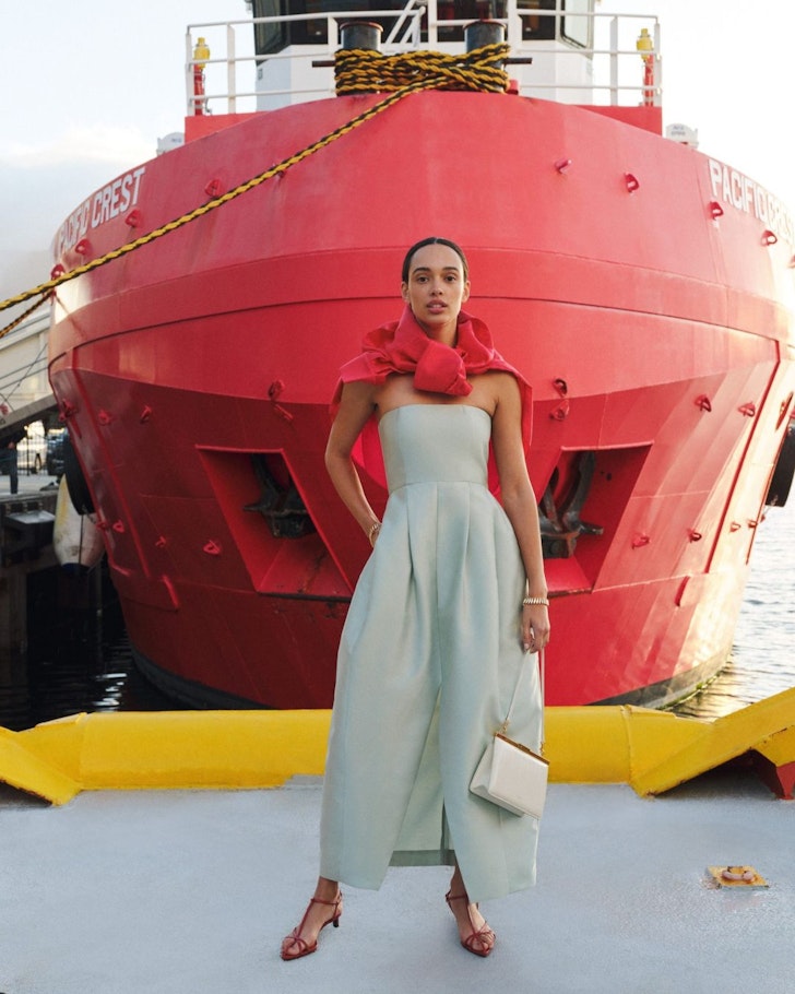 A woman stands in front of a pink boat wearing an outfit and bag from Oroton one of the best Australian fashion brands