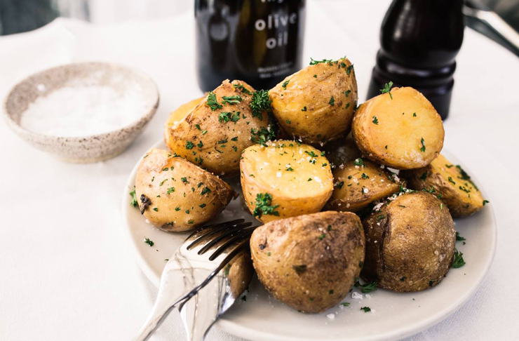Delicious, crispy potatoes sit on a plate with a bottle of olive oil in the background