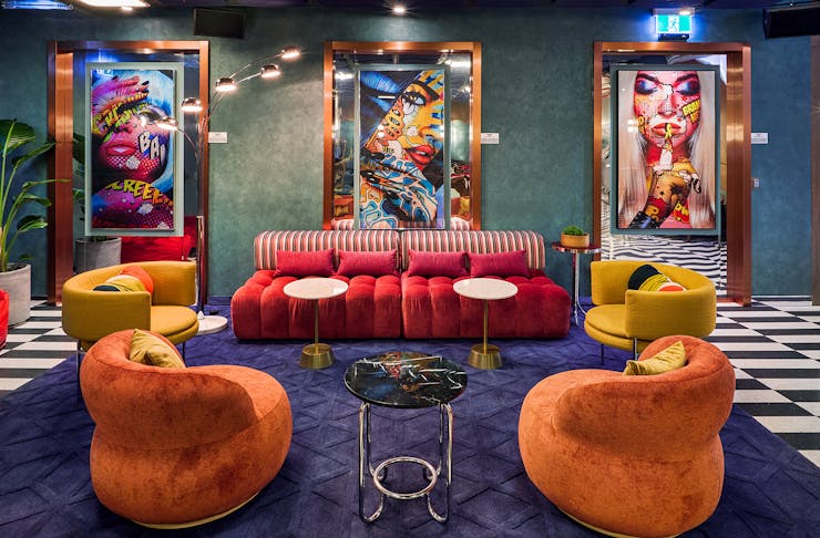 A groovy lounge area with colourful plush couches surrounded by pop art. 