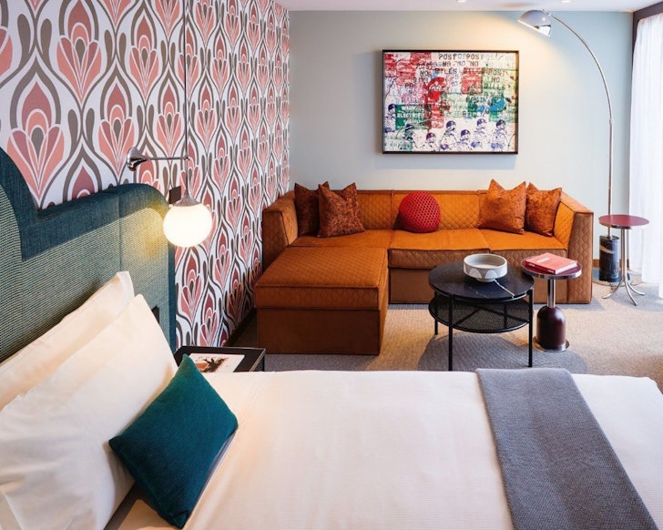 A bedroom with statement wallpaper and an orange couch at Ovolo South Yarra one of the best hotels in Australia