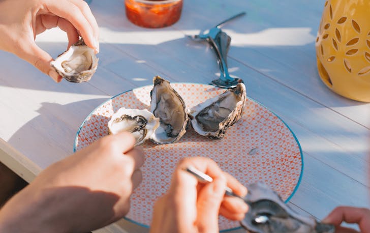 A plate of oysters with people shucking. 