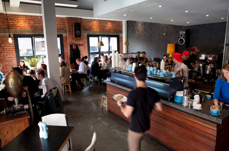 A bustling shot of the best cafes melbourne has with waiters carrying dishes.