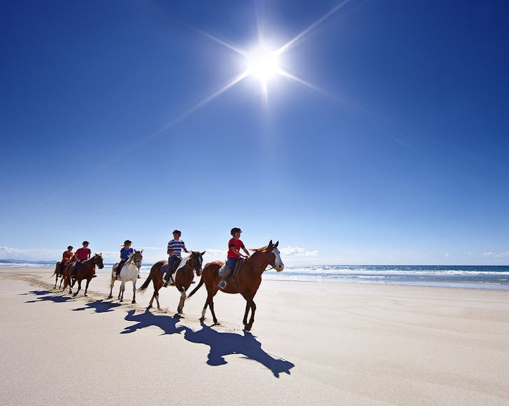 People ride on horseback on Pakiri beach.