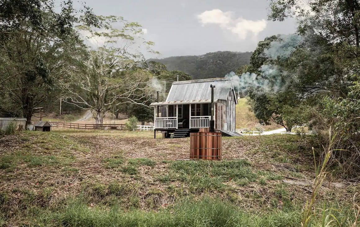 small rustic looking house in the bush with a spa outside