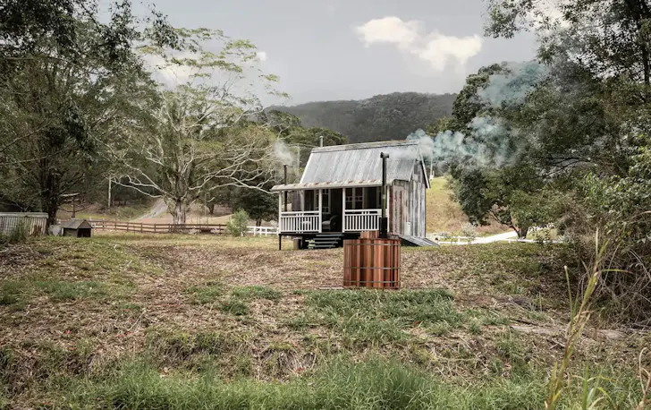 small rustic looking house in the bush with a spa outside