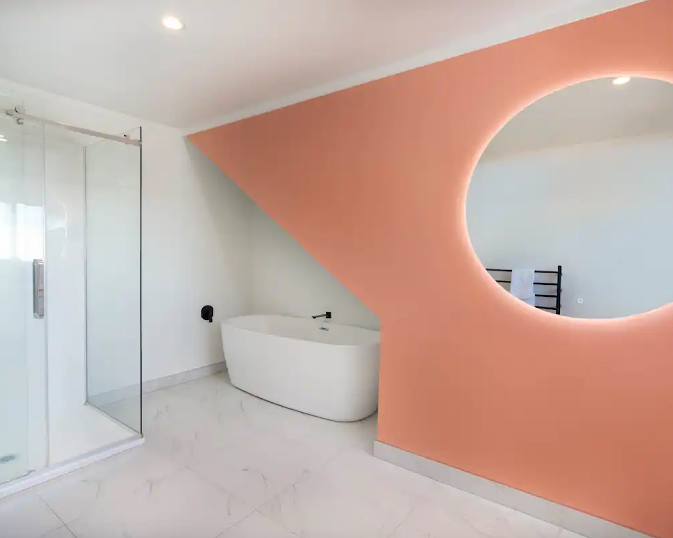 A chic white bathtub is tucked under a peach, geometric feature wall in a bathroom in one of the best Airbnbs in Taupo. 