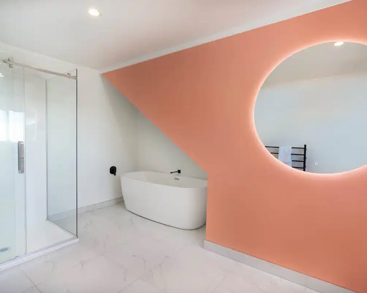 A chic white bathtub is tucked under a peach, geometric feature wall in a bathroom in one of the best Airbnbs in Taupo. 