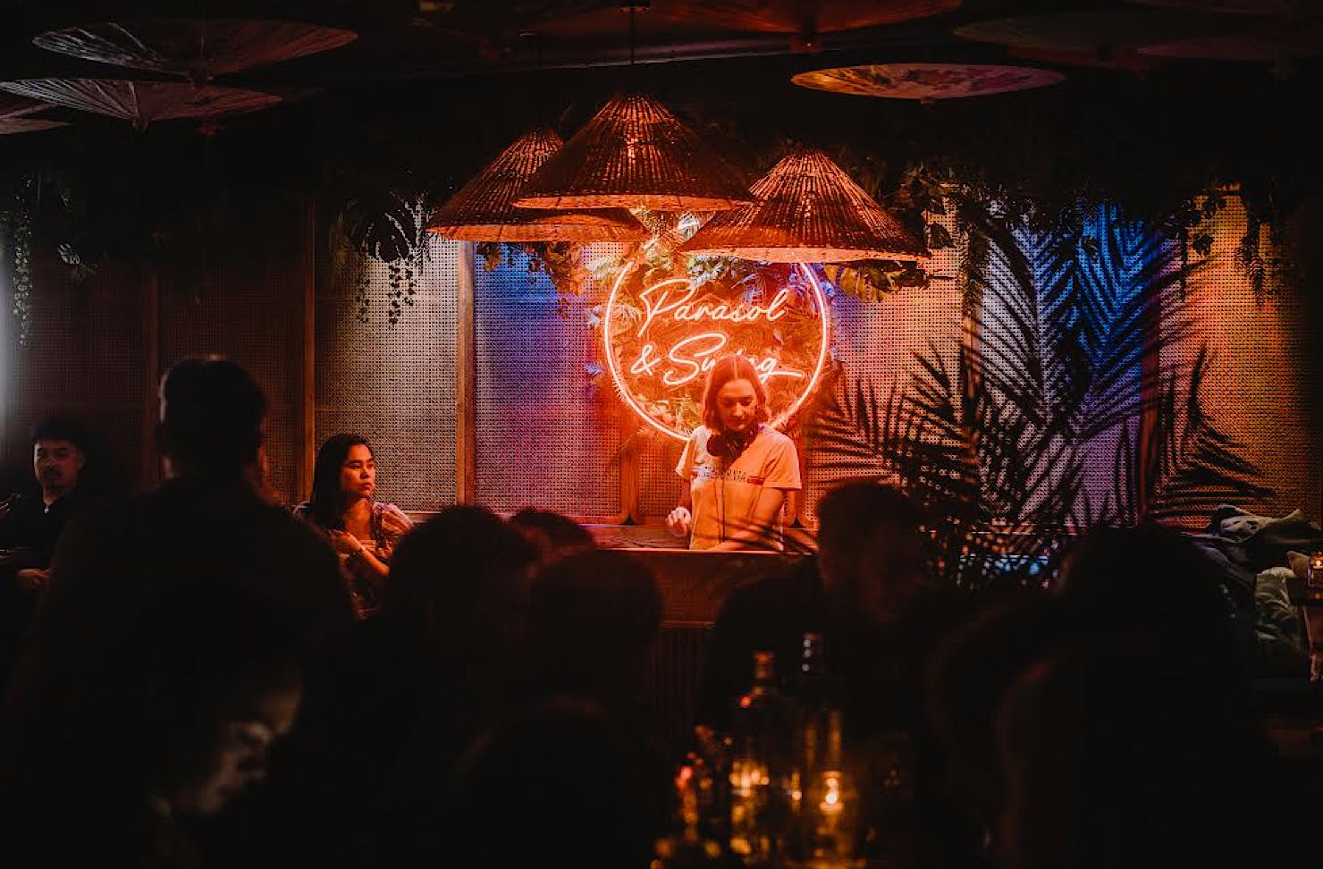 A DJ plays a set in front of an orange neon wall decal of the words Parasol and Swing. 