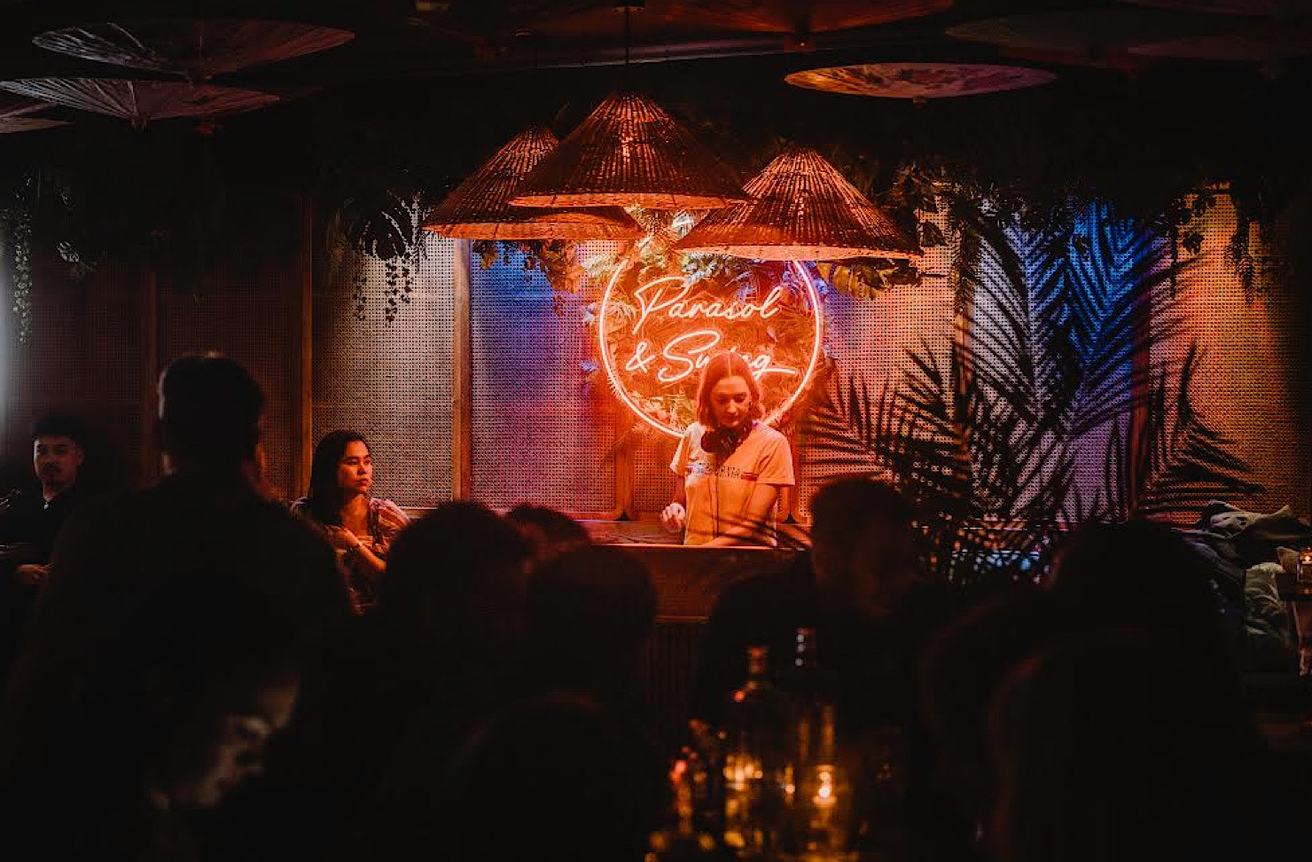 A DJ plays a set in front of an orange neon wall decal of the words Parasol and Swing. 