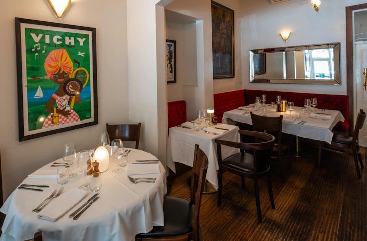 Three white-clothed tables sit in a dining room with french art and mirrors adoring the walls at one of the best french restaurants Melbourne has to offer.