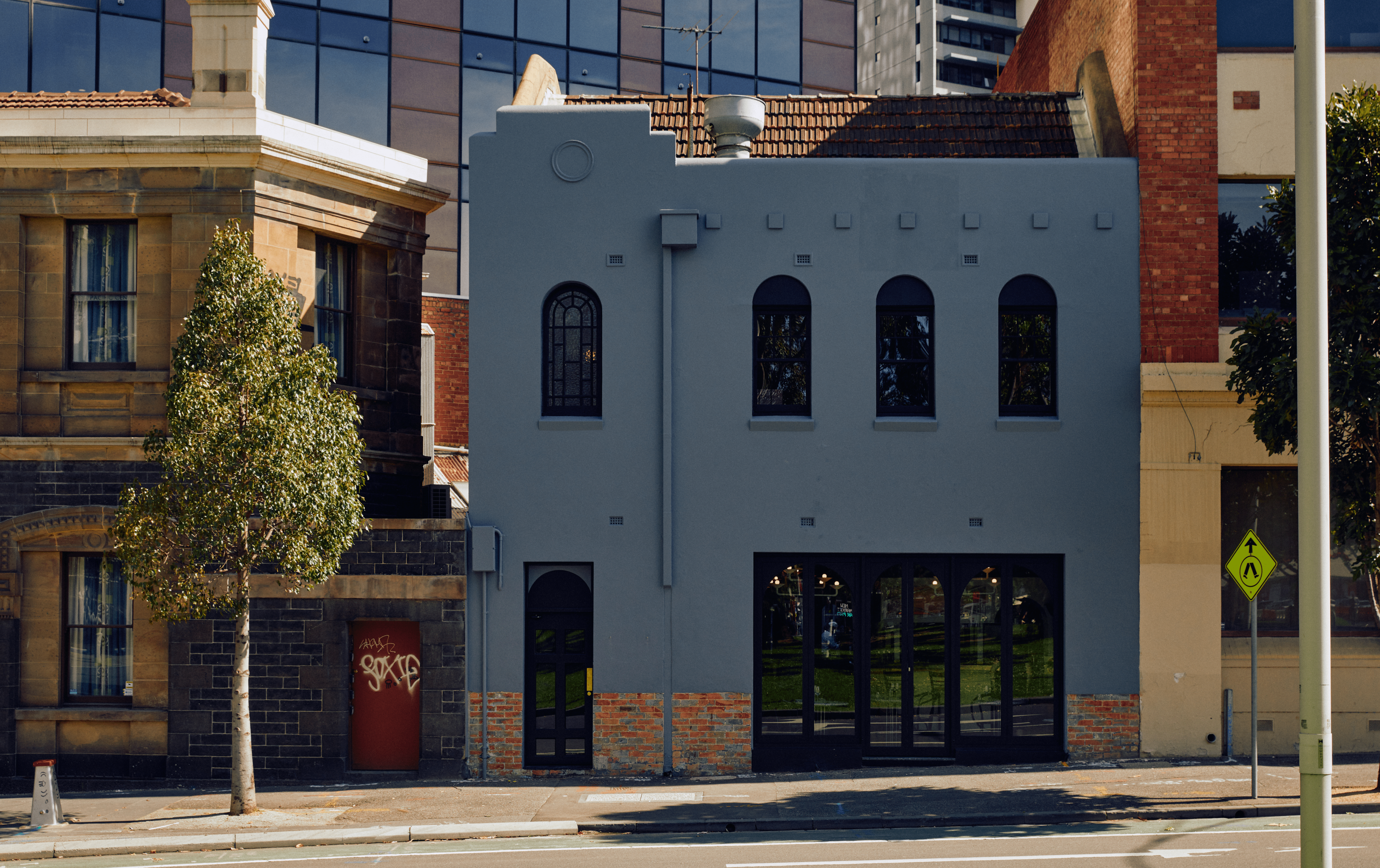 The front exterior of Patsys, a blueish grey building with arched windows and glass door. 