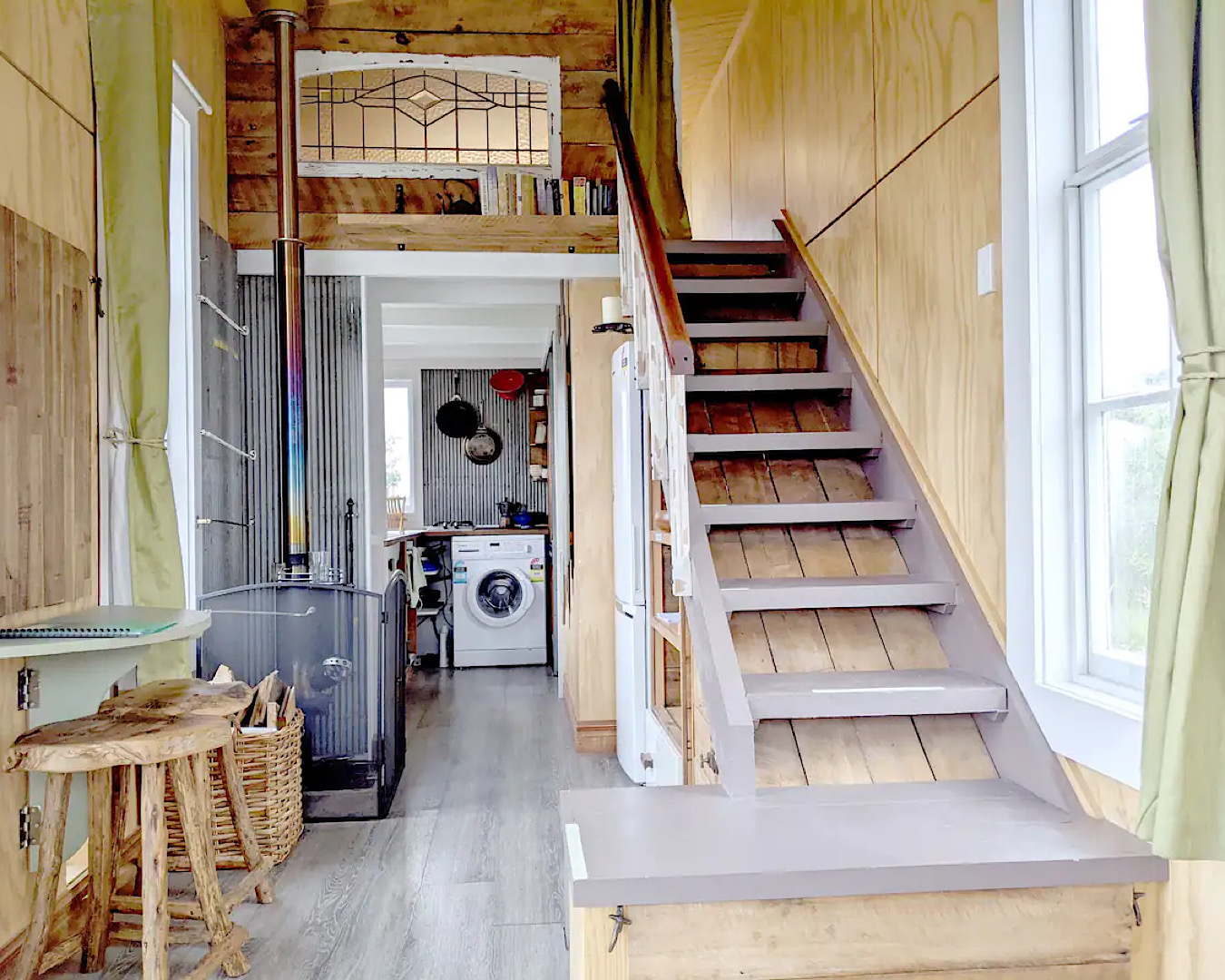 A staircase leading up to a loft bed and the view through to a washing machine at a peaceful tiny house in Fairlie. 