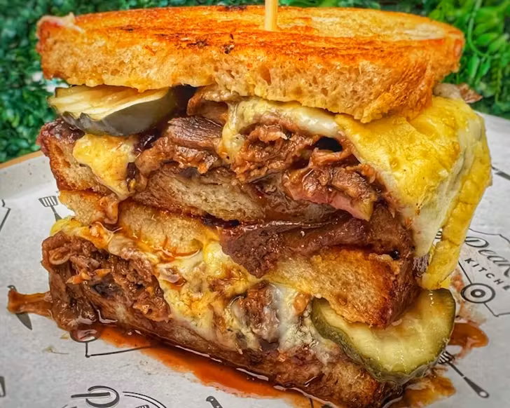 A hefty toasted sandwich brimming with low and slow beef, sliced pickles, and copious amounts of cheese. 