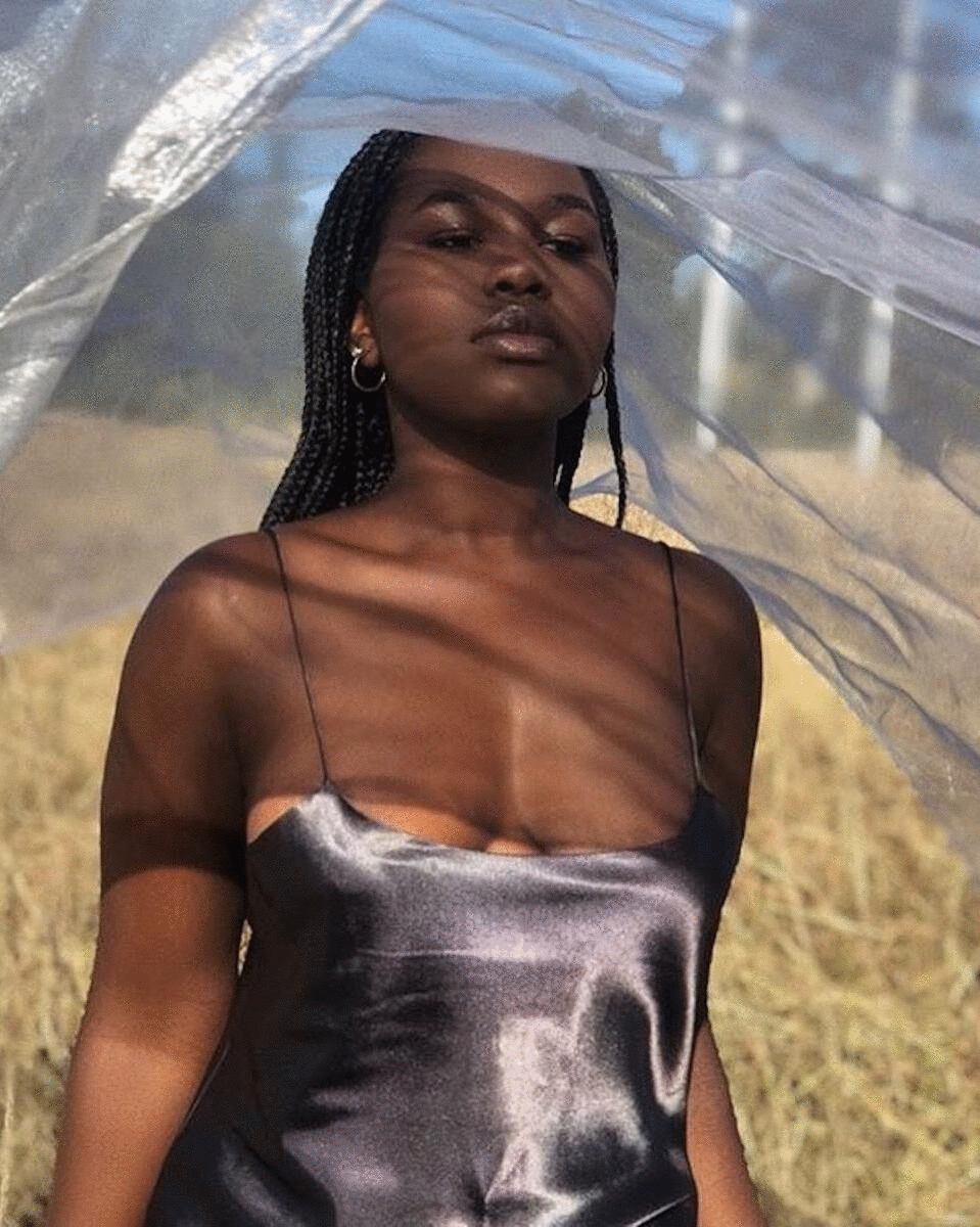 A beautiful black woman stands in a field wearing a slinky slip dress.