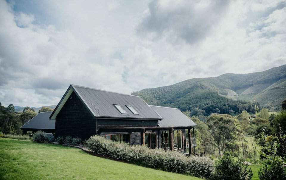 A house on a hill before the snow mountains in Victoria with a black roof. 