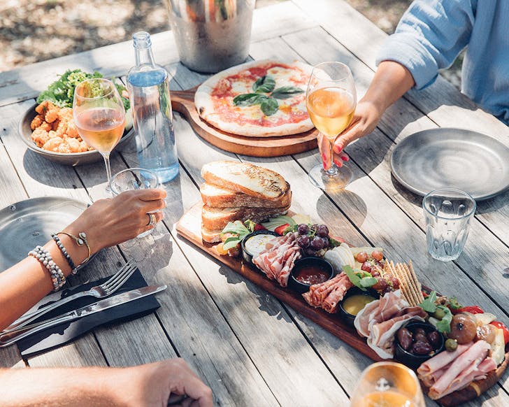 People sitting at a rustic table with food and wine at Man O War, Waiheke Island.