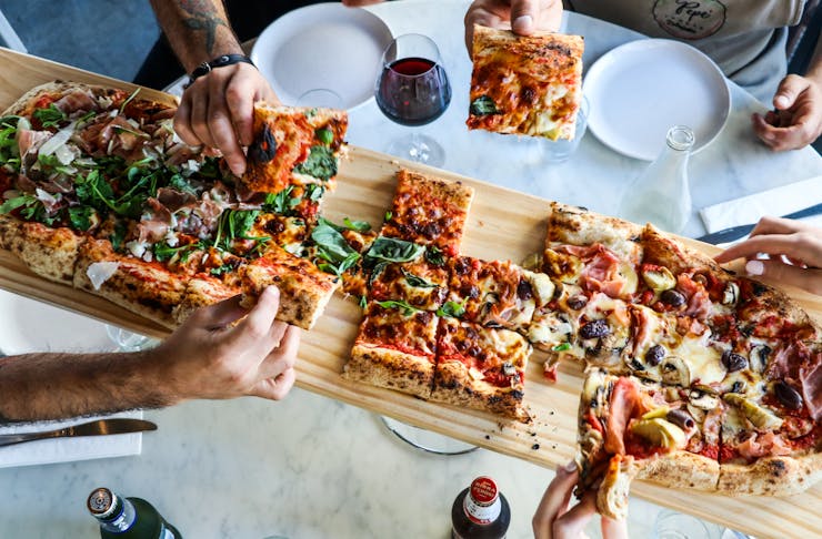 Hands grabbing slices of a one-metre pizza.