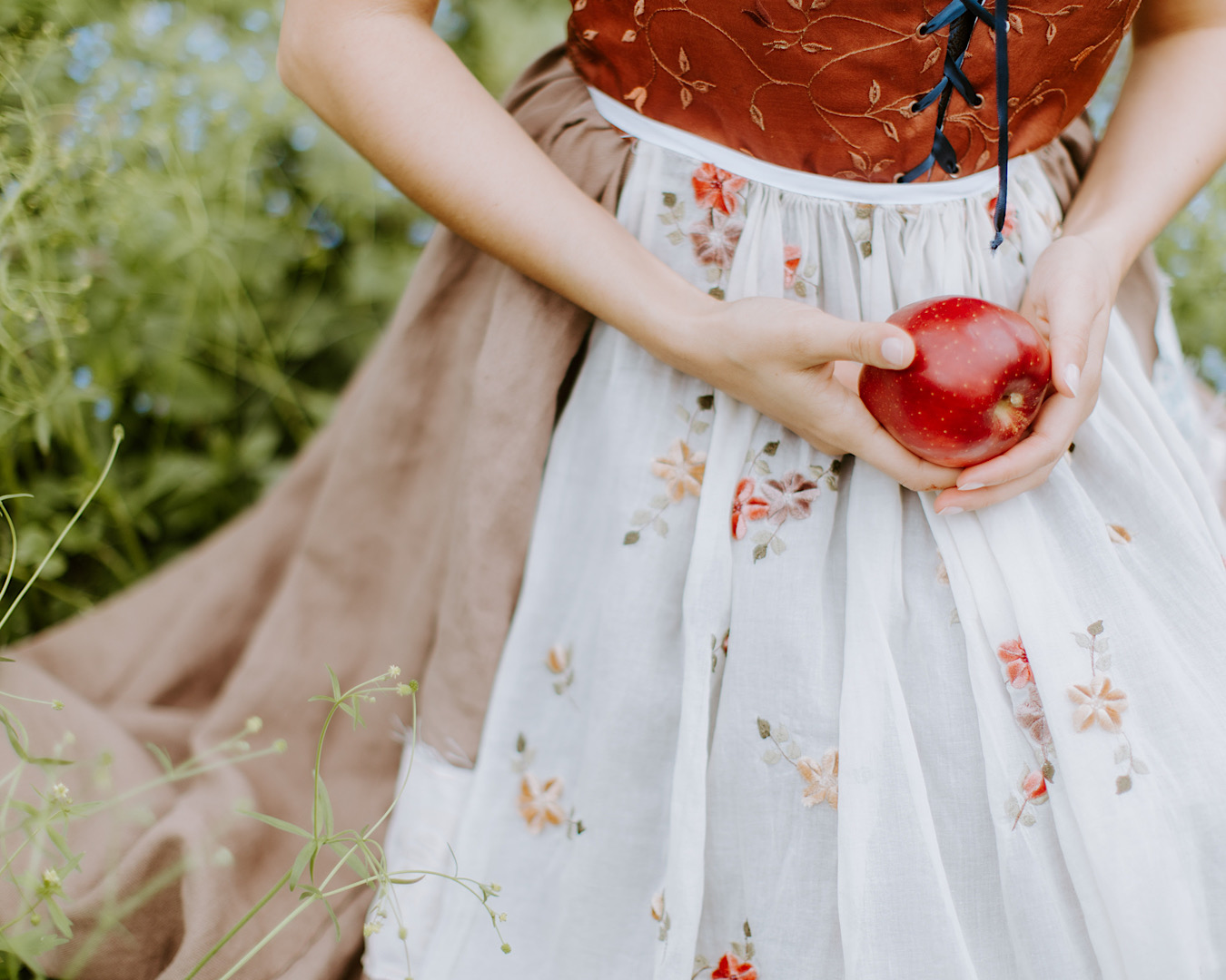 Person kneeling wearing a costume reminiscent of Snow White and holding a red apple. 