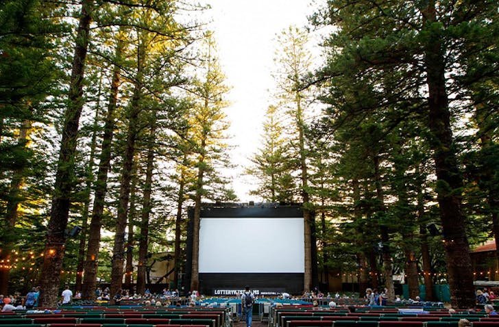 A huge cinema screen sits outside among cascading talls.