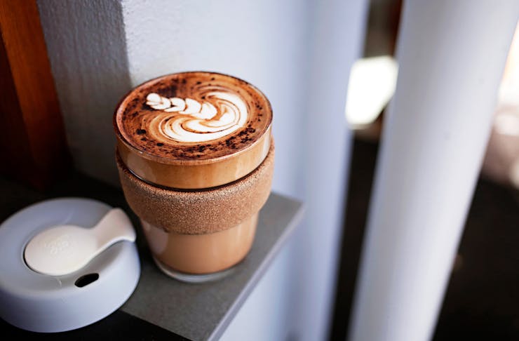 A KeepCup on a bench with the lid off, filled with a latte.